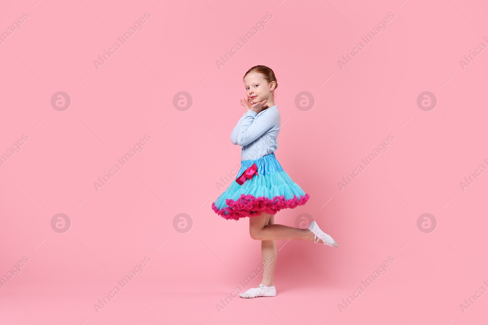 Photo of Cute little girl dancing on pink background