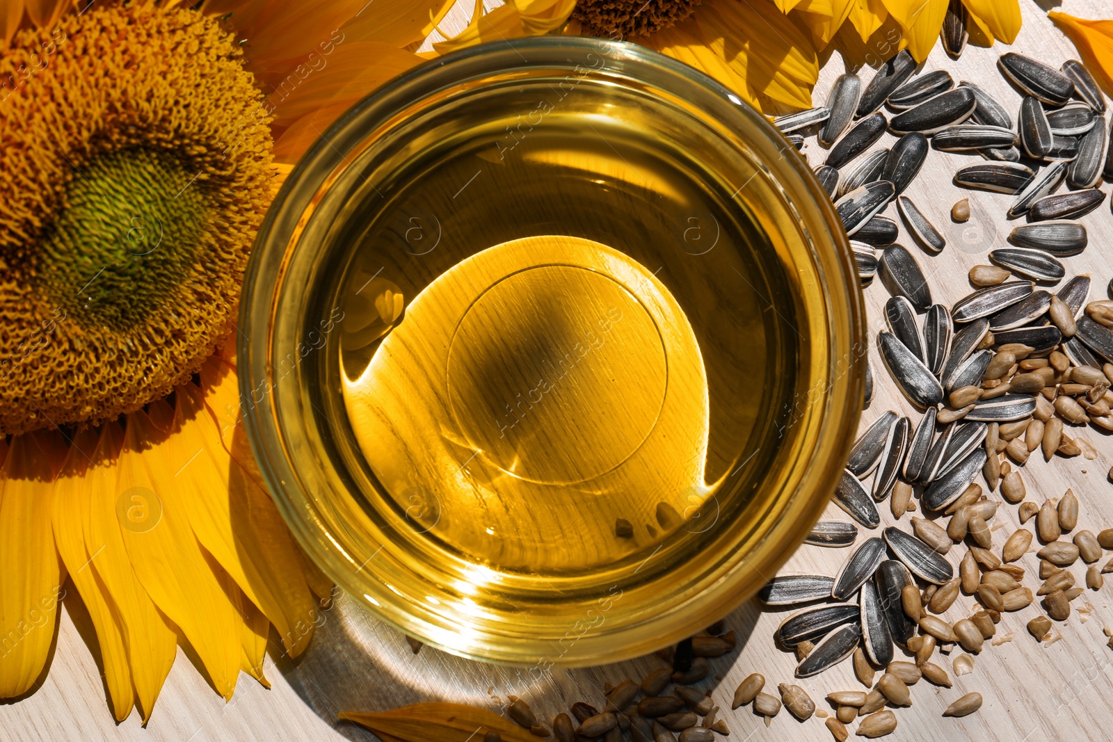 Photo of Sunflower oil in glass bowl and seeds on wooden table, flat lay