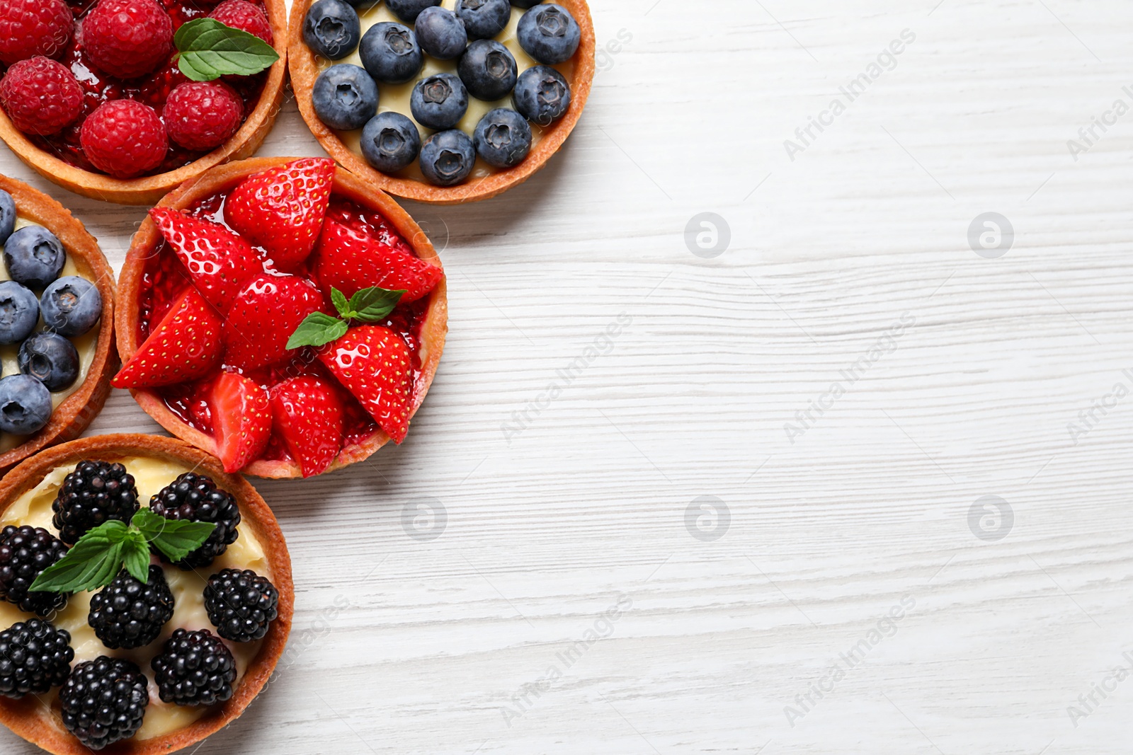 Photo of Tartlets with different fresh berries on white wooden table, flat lay and space for text. Delicious dessert
