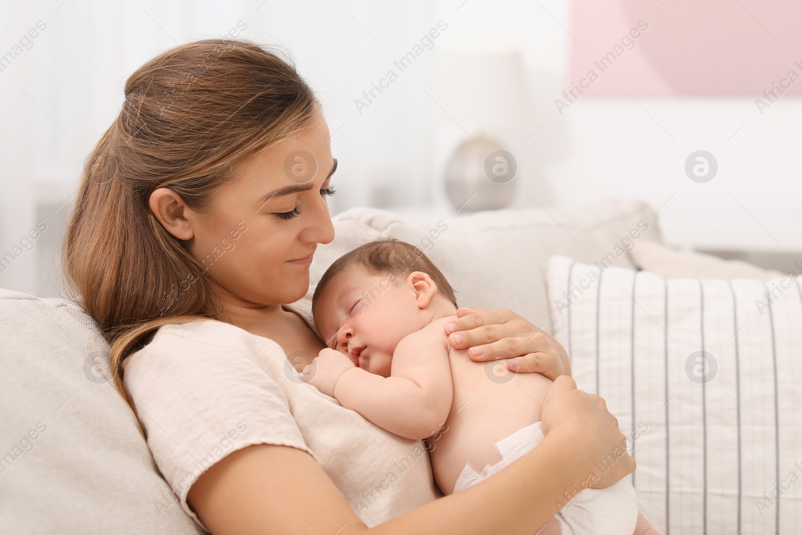 Photo of Mother holding her cute newborn baby on sofa indoors