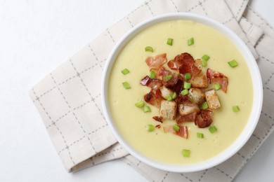 Tasty potato soup with bacon, green onion and croutons in bowl on white table, top view. Space for text