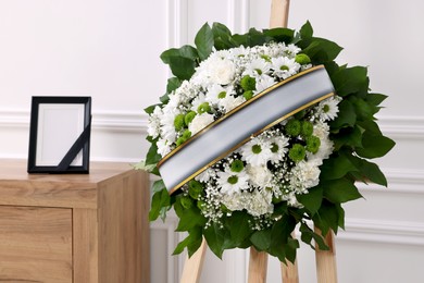 Photo of Wreath of flowers and photo frame with black ribbon on commode in room. Funeral attributes