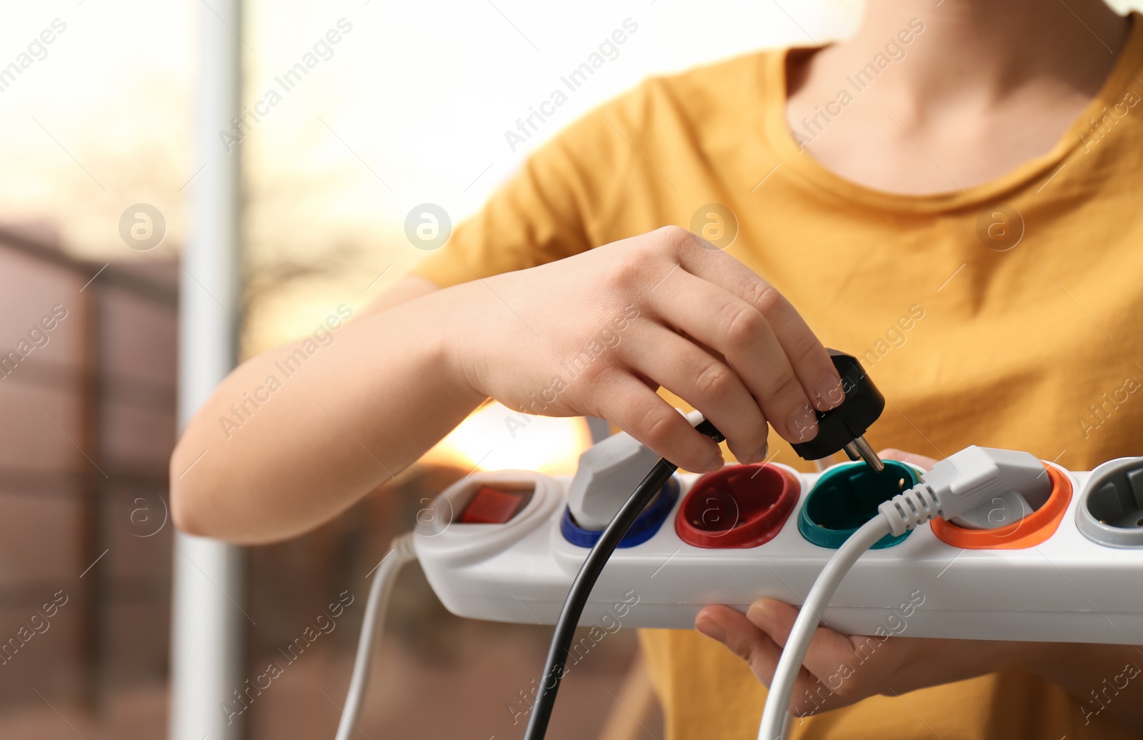 Photo of Woman inserting power plug into extension cord indoors, closeup. Electrician's professional equipment