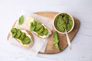 Tasty bruschettas with cream cheese, pesto sauce and fresh basil on white textured table, top view