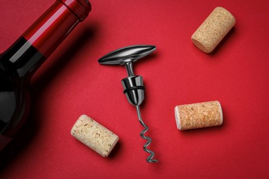 Photo of Corkscrew with wine bottle and stoppers on red background, flat lay
