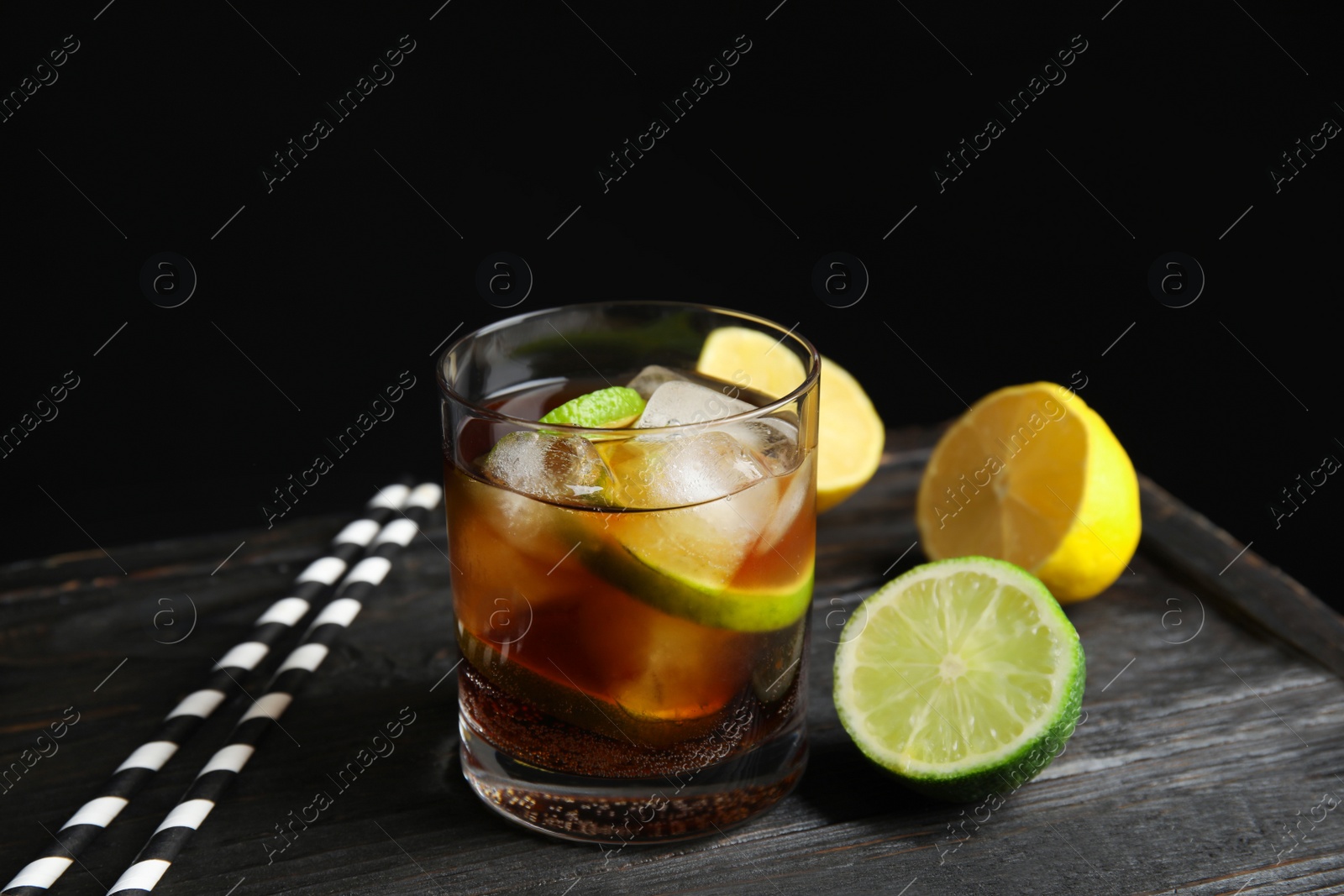 Photo of Glass of cocktail with cola, ice and cut lime on table against black background