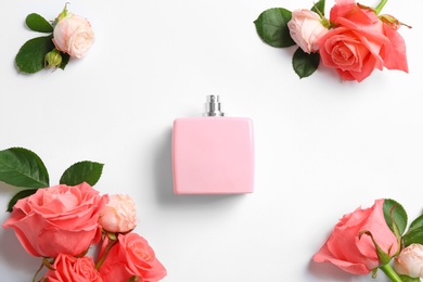 Bottle of perfume and roses on white background, top view