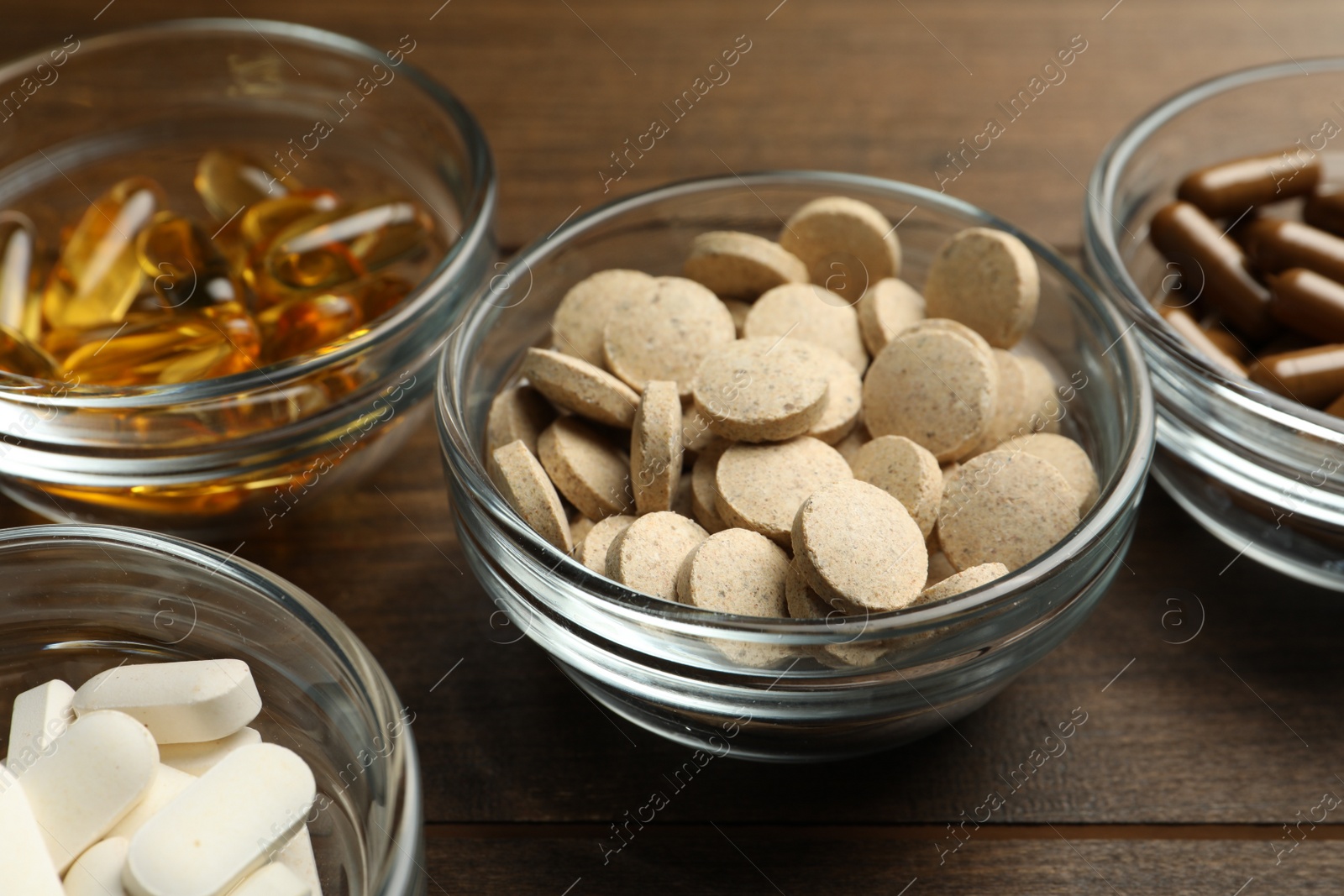 Photo of Different dietary supplements in glass bowls on wooden table, closeup