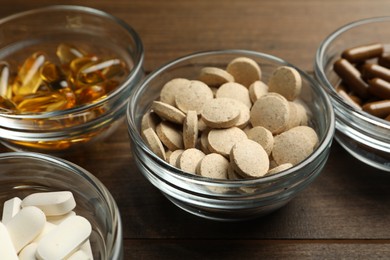 Photo of Different dietary supplements in glass bowls on wooden table, closeup