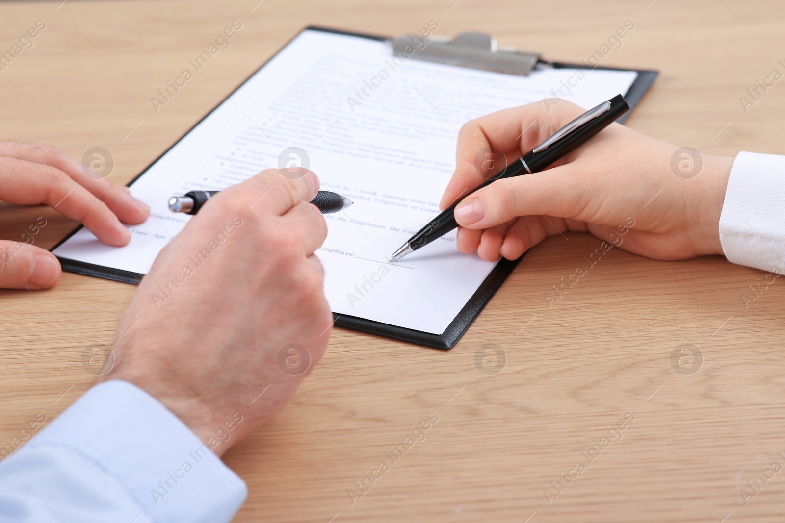 Photo of Businesspeople signing contract at wooden table, closeup of hands