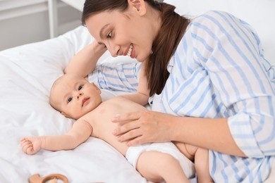 Happy young woman applying body cream onto baby`s skin on bed