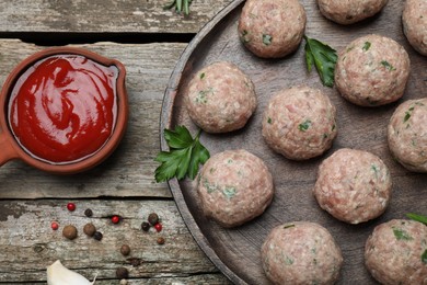 Photo of Many fresh raw meatballs and ketchup on wooden table, flat lay