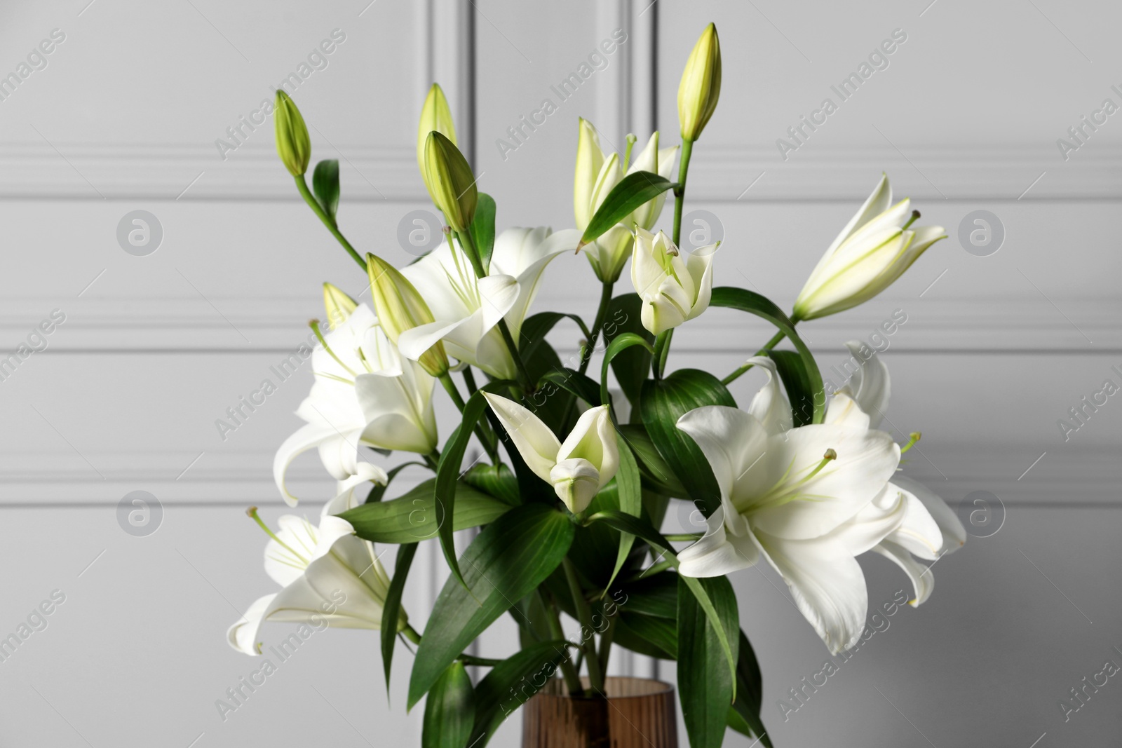 Photo of Beautiful bouquet of lily flowers in glass vase near light grey wall