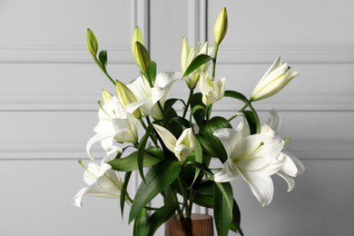 Photo of Beautiful bouquet of lily flowers in glass vase near light grey wall