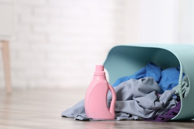 Photo of Detergent and laundry basket with dirty clothes on floor indoors. Space for text