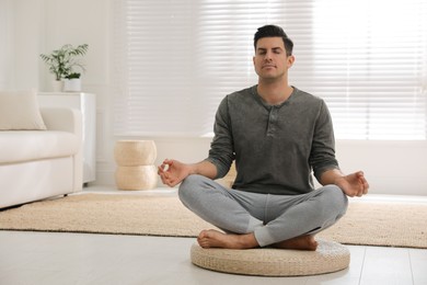 Photo of Man meditating on wicker mat at home. Space for text