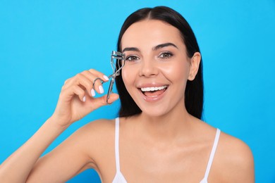 Photo of Beautiful young woman using eyelash curler on light blue background