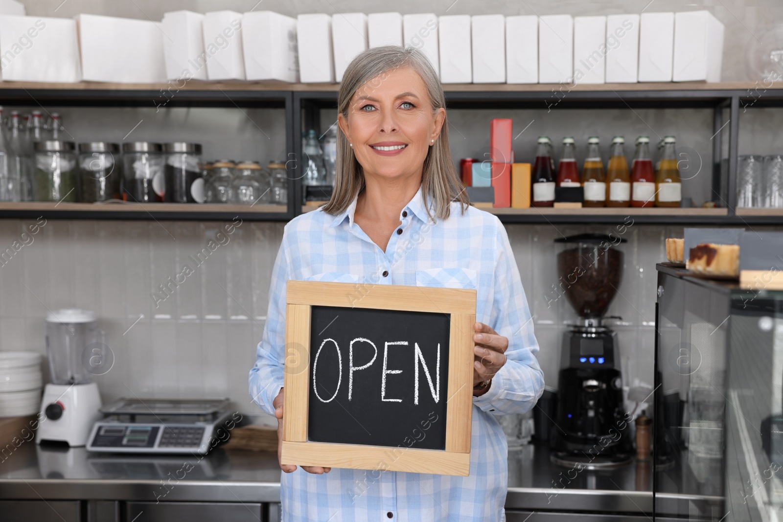 Photo of Happy business owner holding open sign in her coffee shop