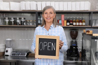 Photo of Happy business owner holding open sign in her coffee shop