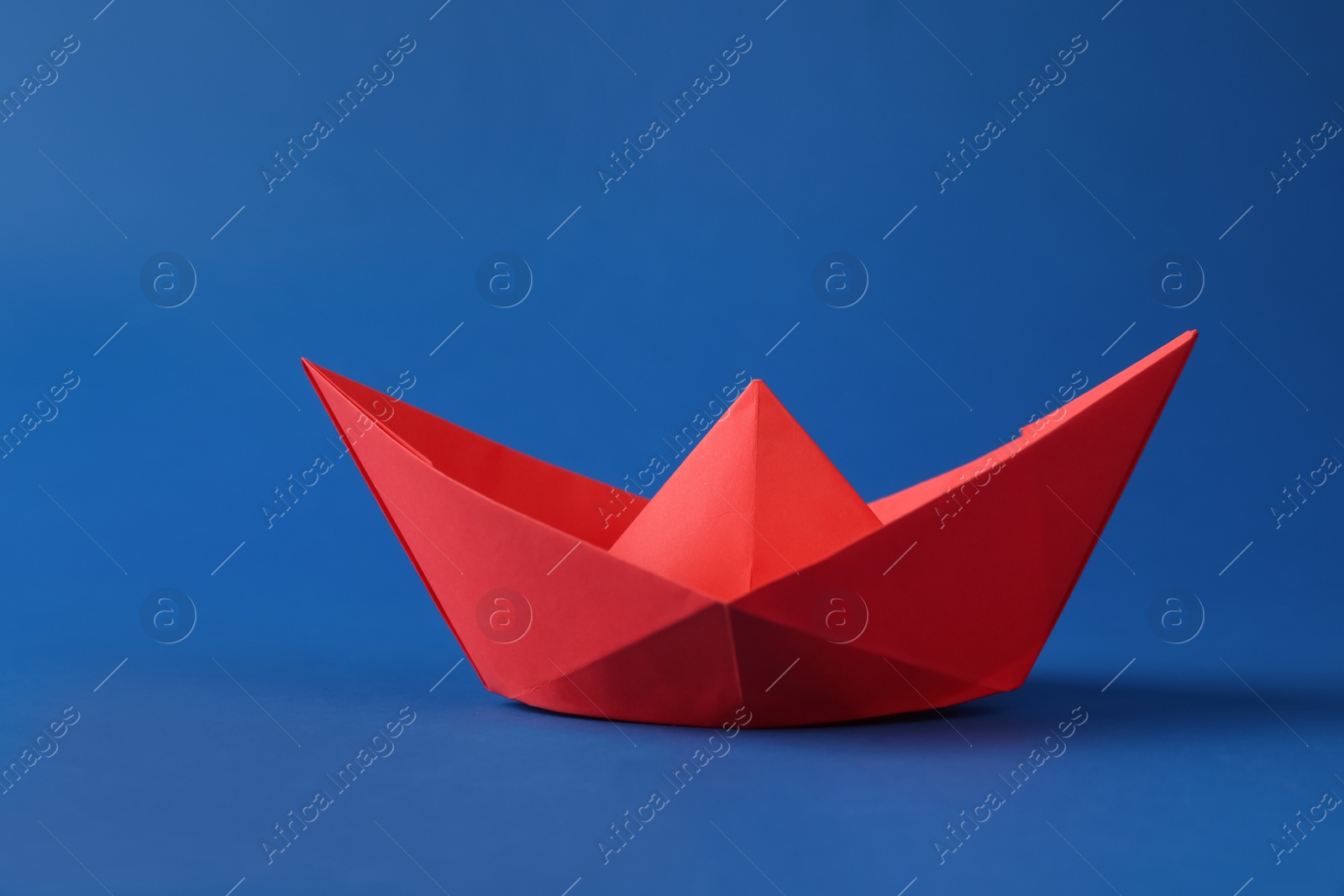 Photo of Handmade red paper boat on blue background. Origami art