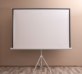 Blank projection screen near beige wall indoors. Space for design