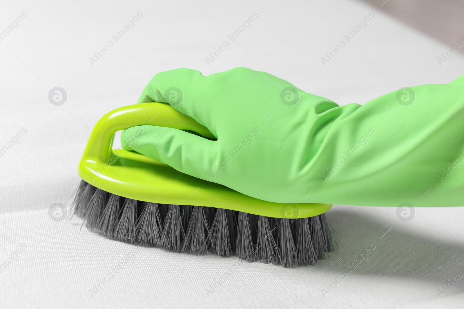 Photo of Woman in green gloves cleaning white mattress with brush, closeup