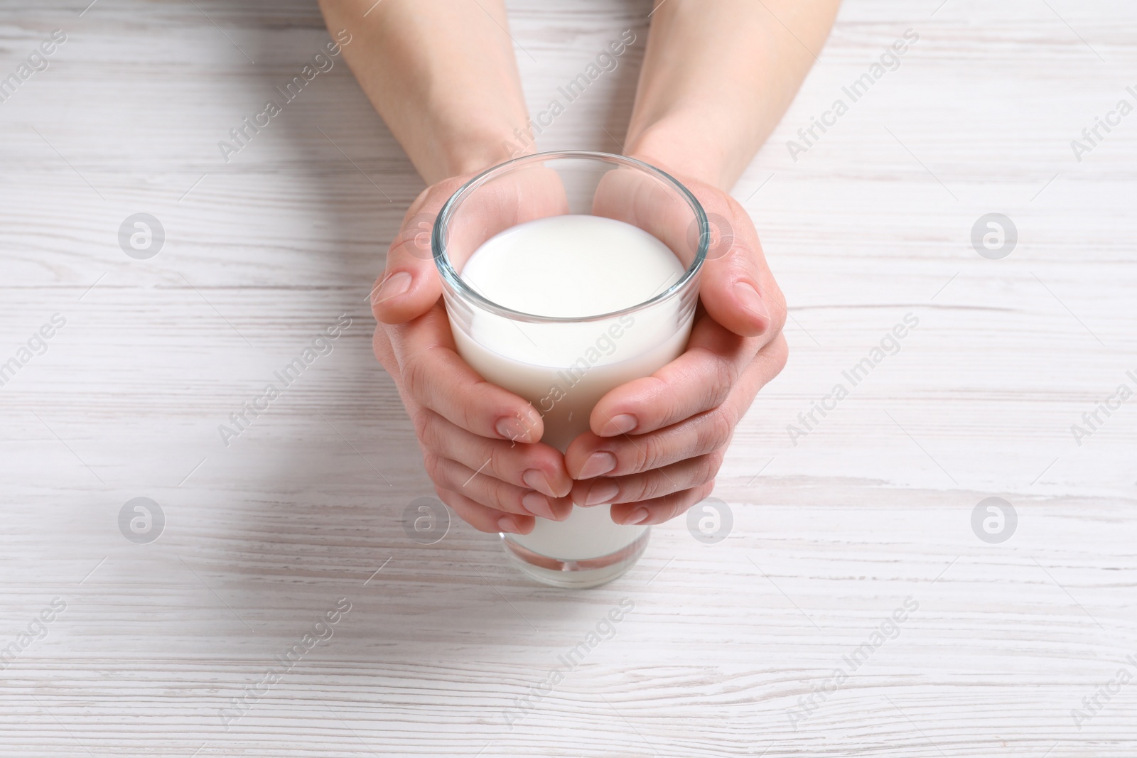 Photo of Woman holding glass of milk at white wooden table, closeup