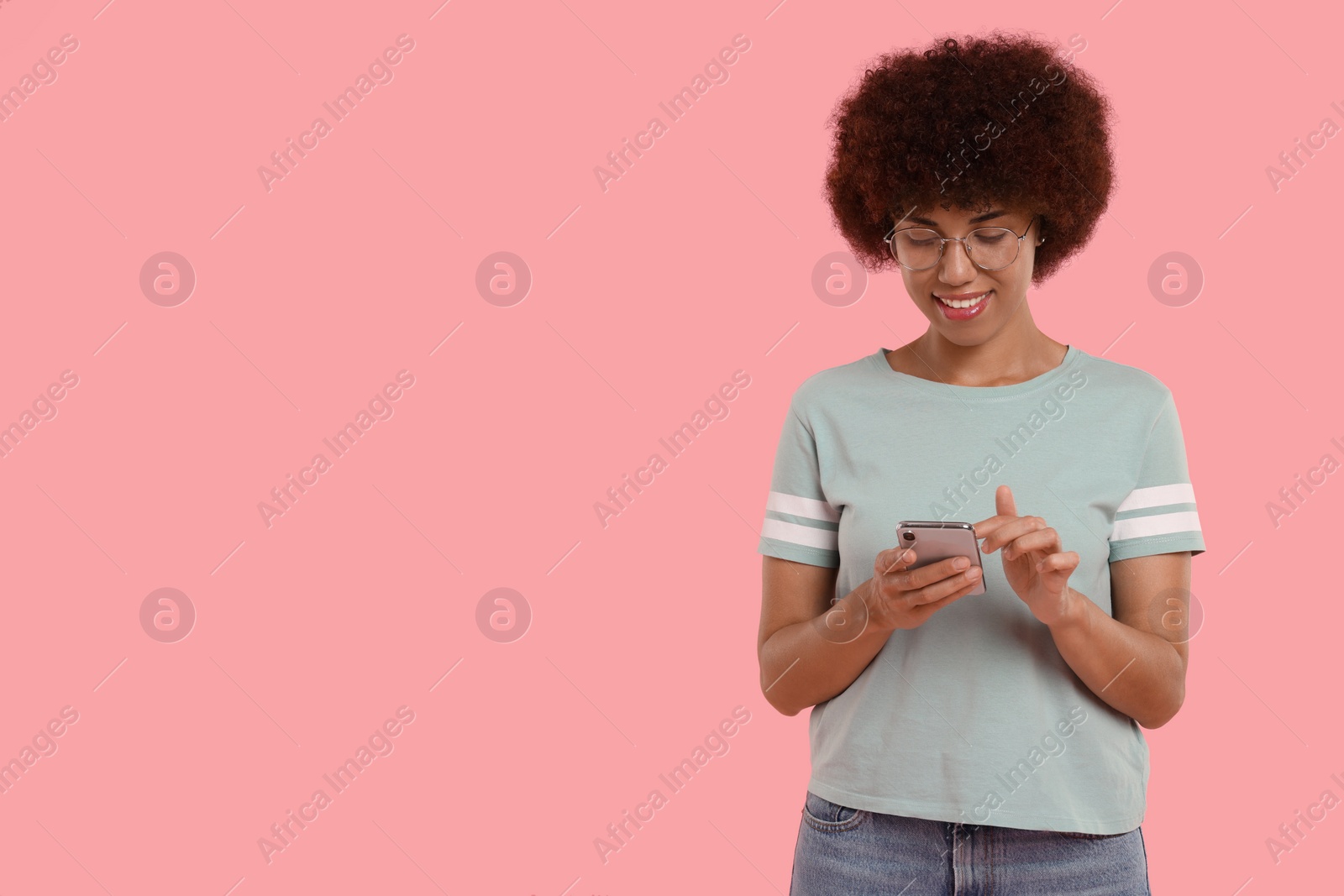 Photo of Young woman in eyeglasses using smartphone on pink background. Space for text