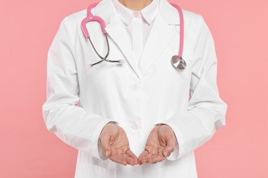 Photo of Doctor with stethoscope holding something on pink background, closeup