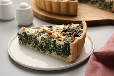 Piece of delicious homemade spinach quiche on light gray table, closeup