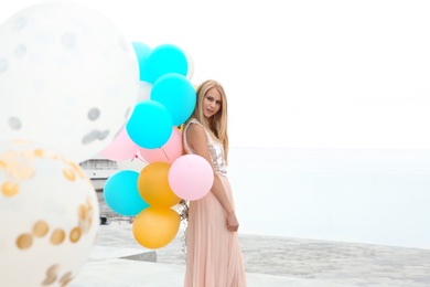 Beautiful young woman with bunch of balloons outdoors. Space for text