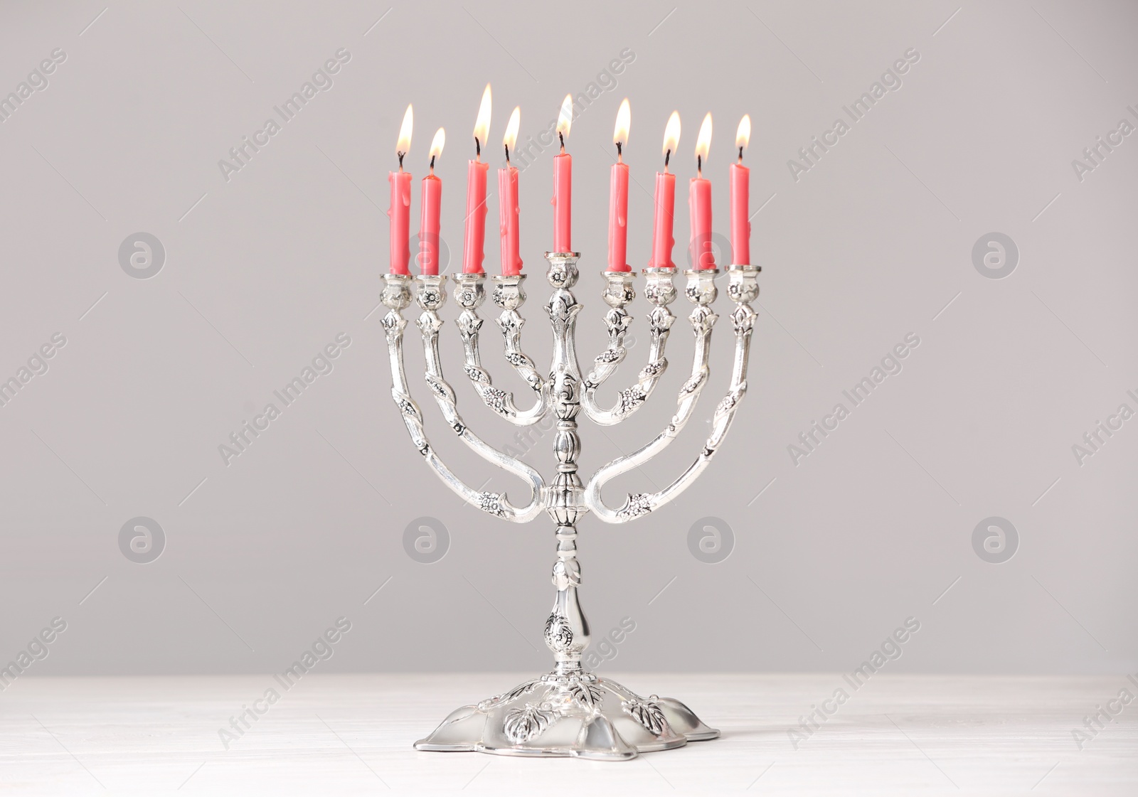 Photo of Silver menorah with burning candles on table against light grey background. Hanukkah celebration