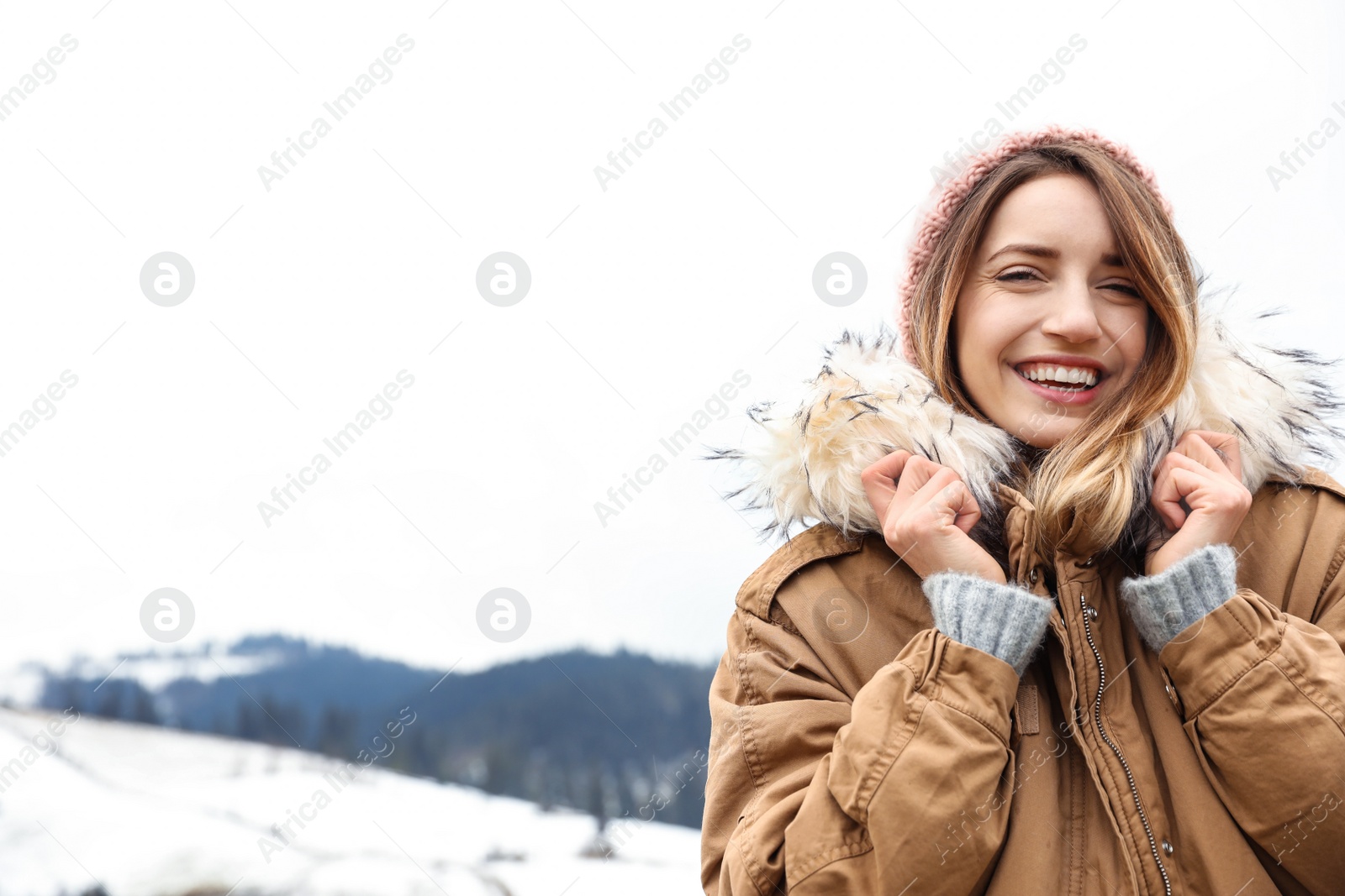 Photo of Young woman in warm clothes near snowy hill, space for text. Winter vacation