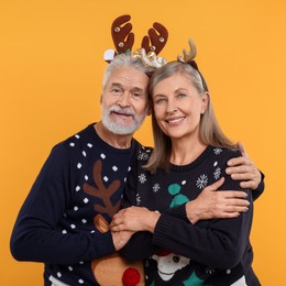 Photo of Senior couple in Christmas sweaters and reindeer headbands on orange background