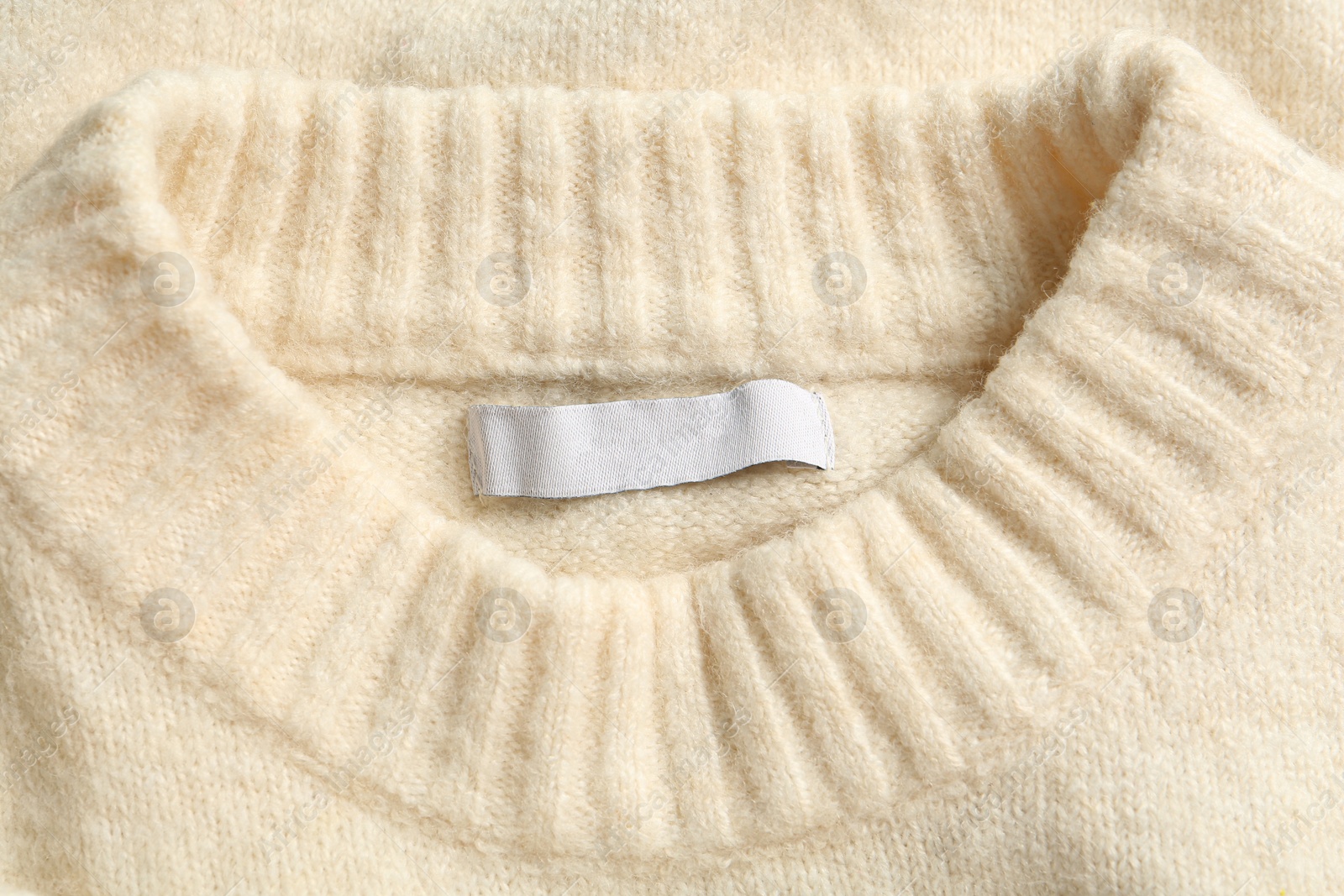 Photo of Blank clothing label on white cashmere sweater, top view
