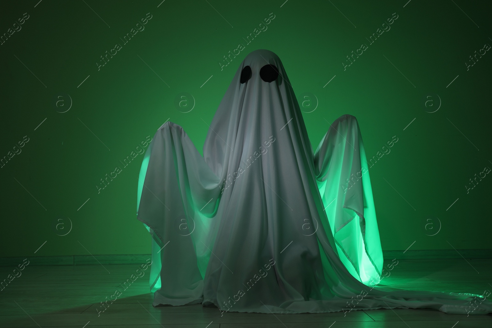 Photo of Creepy ghost. Woman covered with sheet in green light