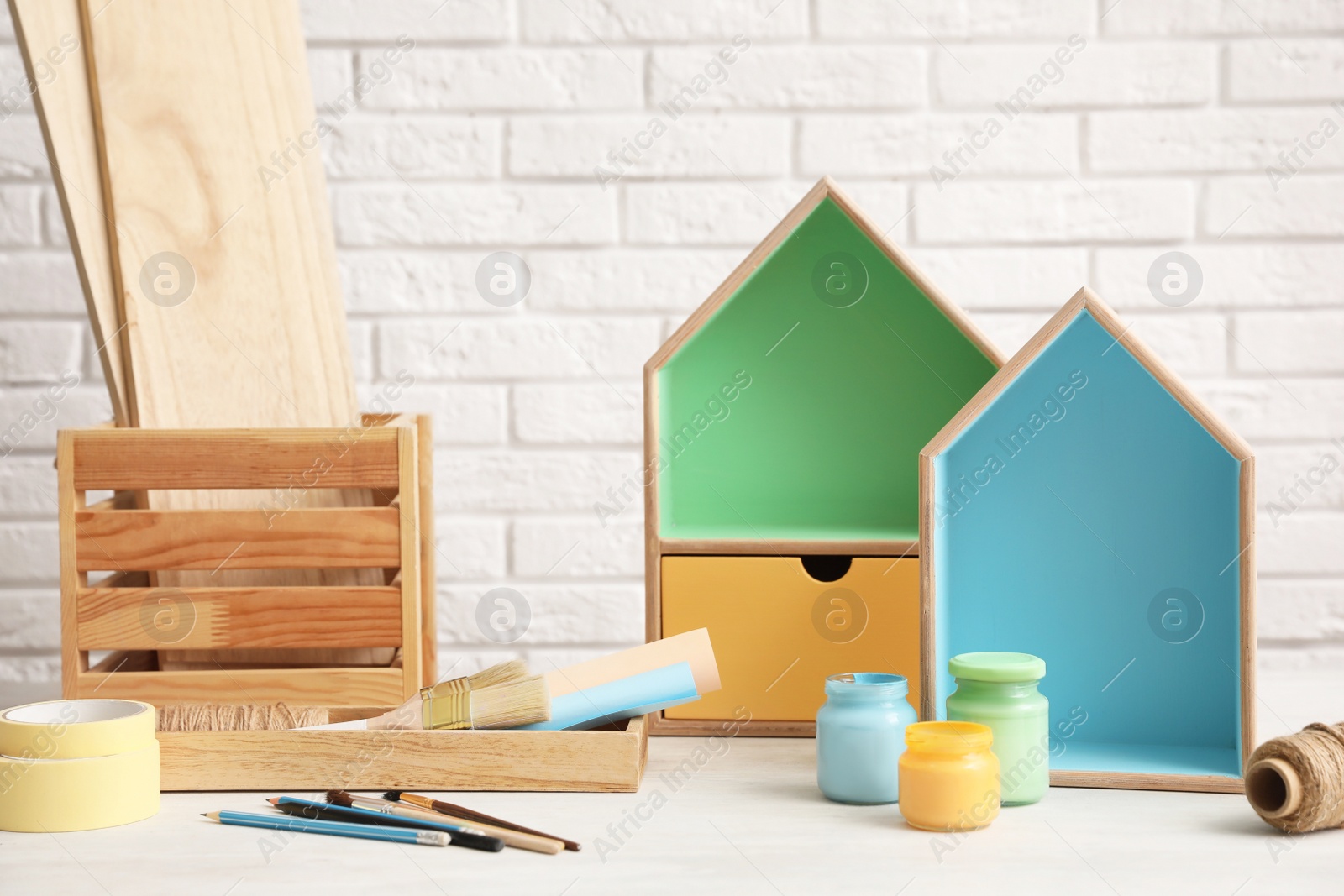 Photo of Composition with house shaped shelves and jars of paints on table against brick wall. Interior elements