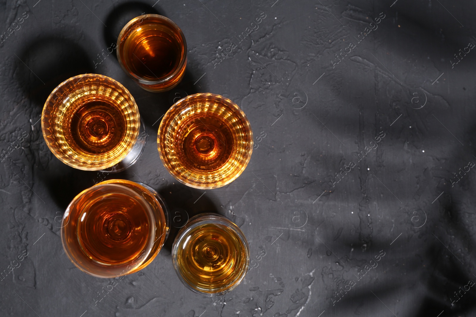 Photo of Many different liqueurs in glasses on dark textured table, flat lay. Space for text