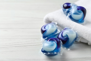 Laundry capsules and towel on white wooden table. Space for text