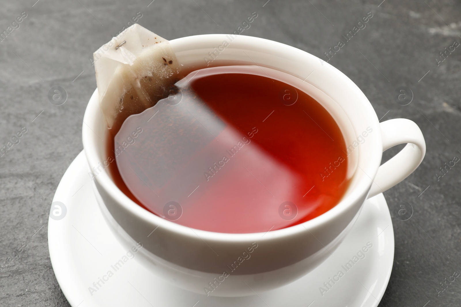 Photo of Tea bag in cup with hot drink on grey textured table, closeup