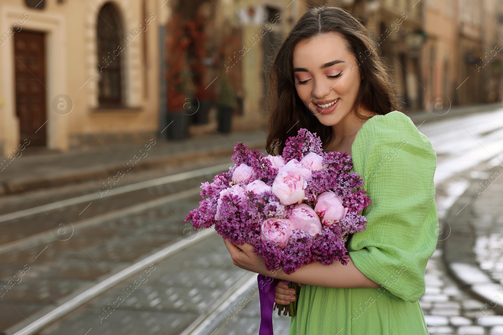 Photo of Beautiful woman with bouquet of spring flowers on city street, space for text