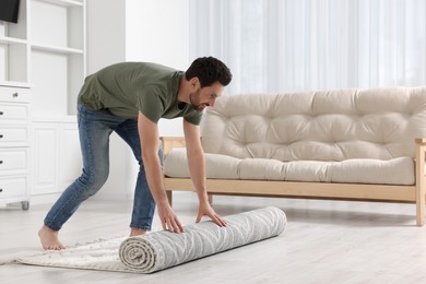 Photo of Smiling man unrolling carpet with beautiful pattern on floor in room, space for text
