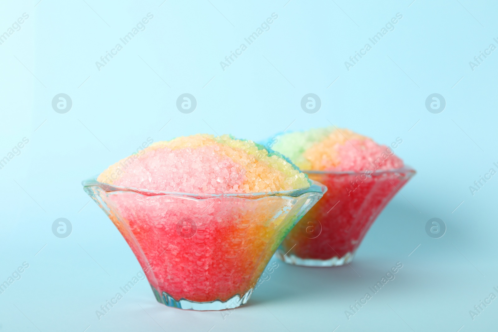 Photo of Rainbow shaving ice in glass dessert bowls on light blue background