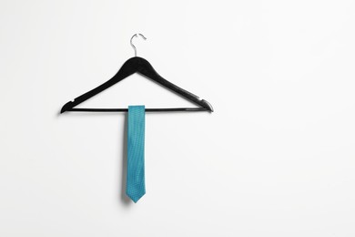 Photo of Hanger with light blue necktie on white wall. Space for text