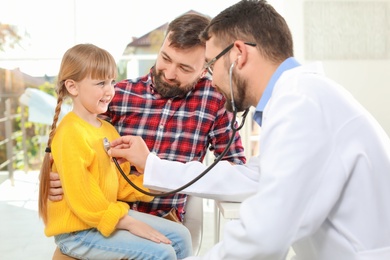 Children's doctor examining little girl with stethoscope in hospital
