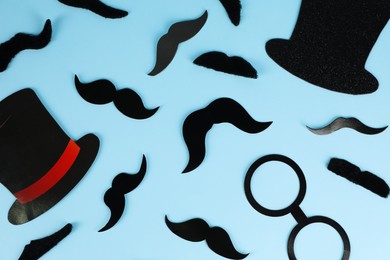 Fake mustaches, hats and glasses on light blue background, flat lay