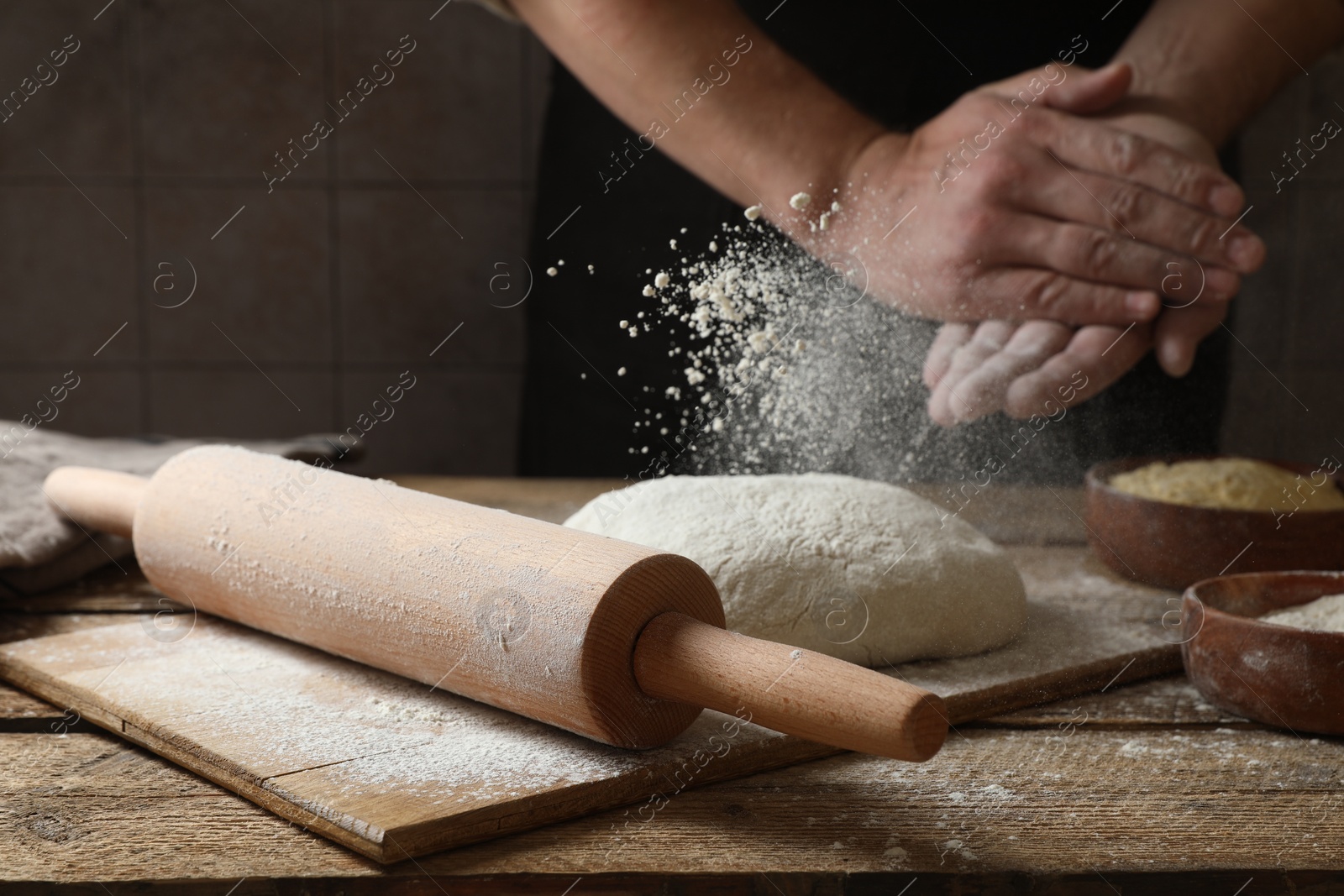 Photo of Man sprinkling flour over dough at wooden table, closeup