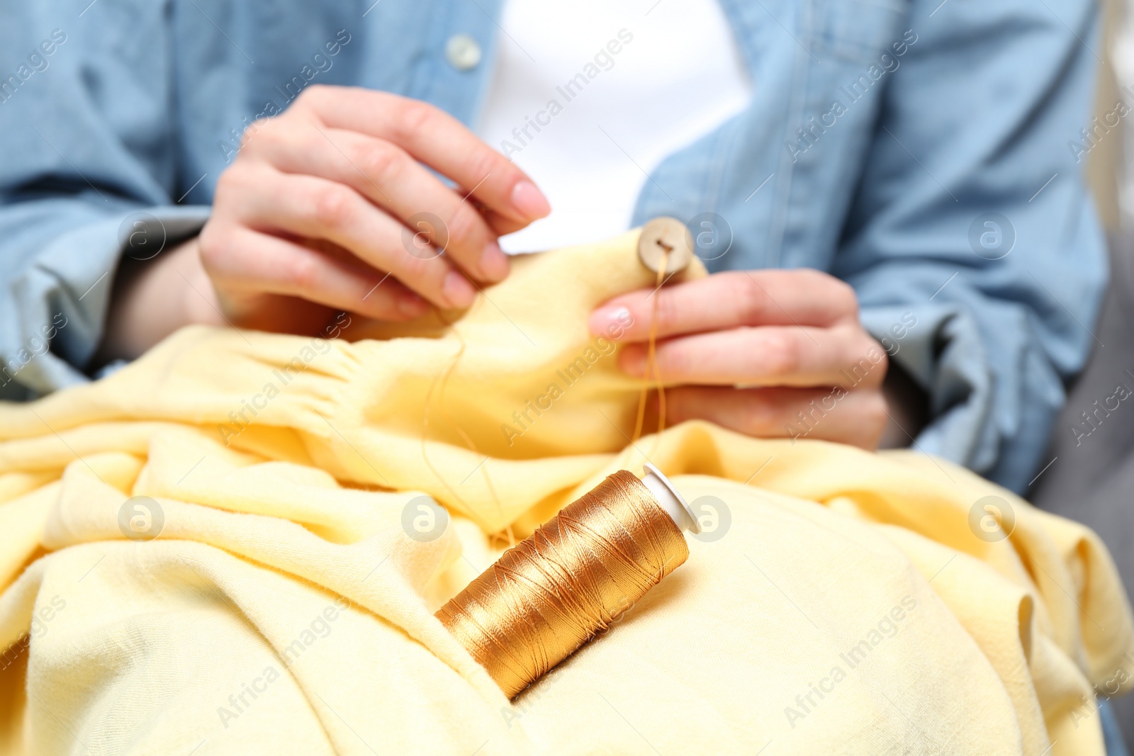 Photo of Woman sewing button onto shirt, focus on thread spool