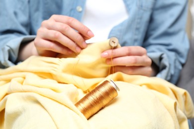 Photo of Woman sewing button onto shirt, focus on thread spool
