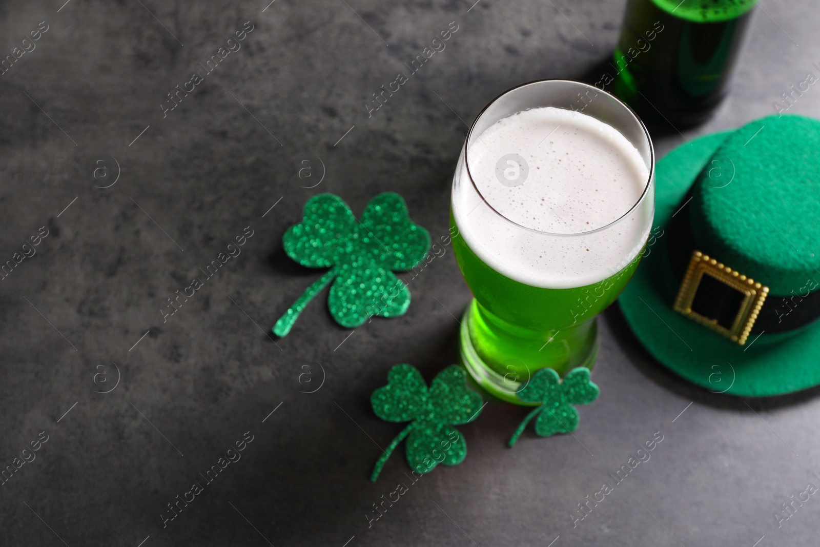 Photo of St. Patrick's day celebration. Green beer, leprechaun hat and decorative clover leaves on grey table. Space for text